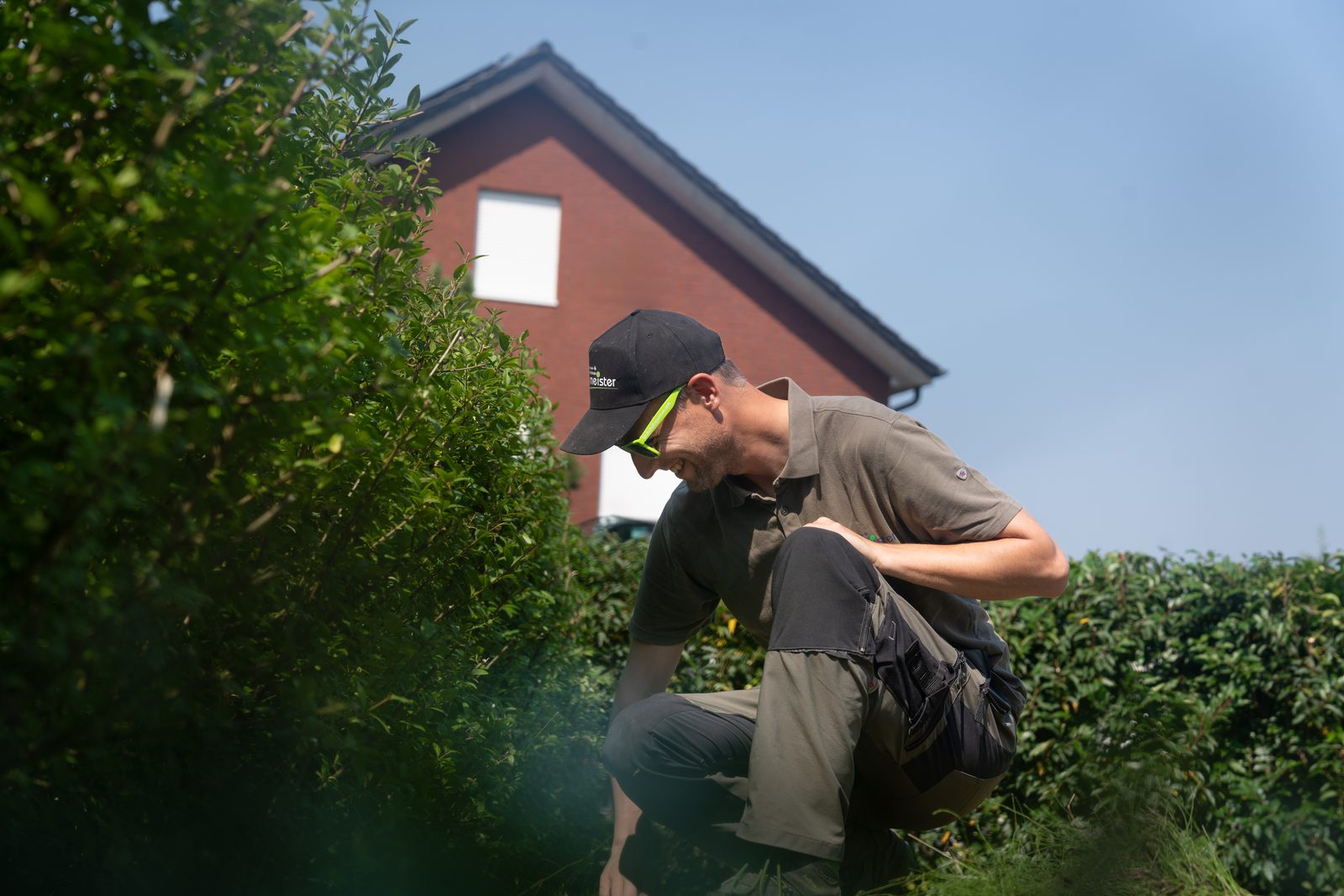 Mitarbeiter arbeitet an einer Hecke in einem Garten